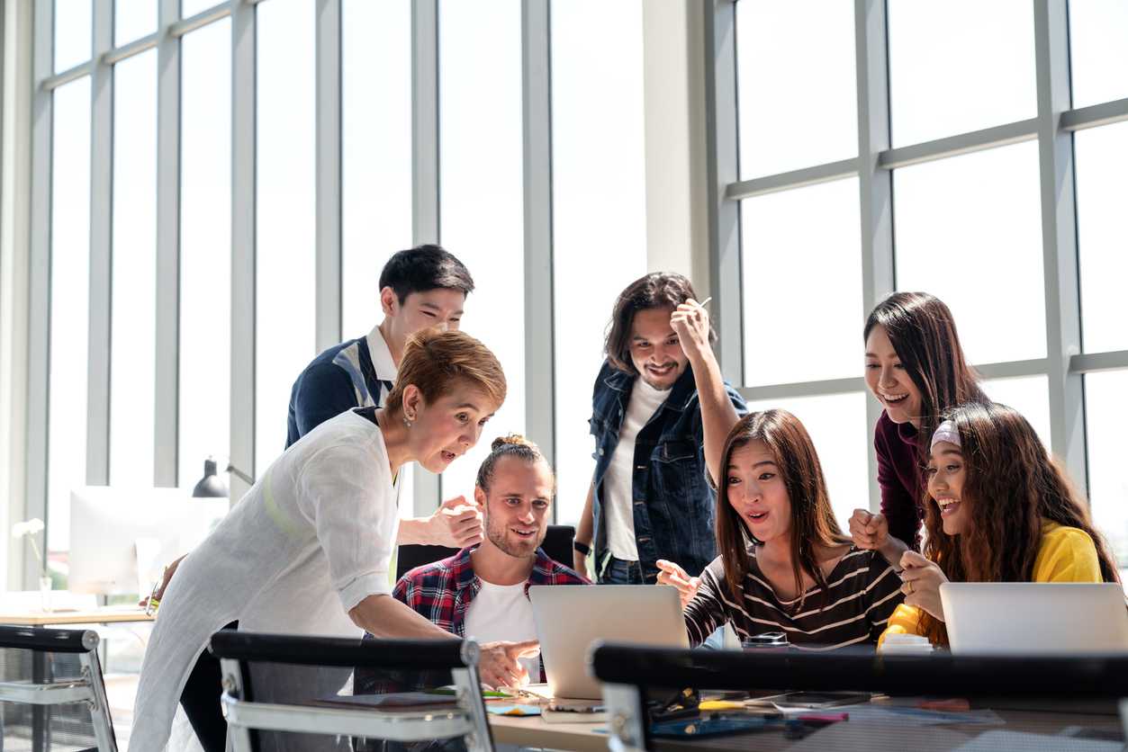 group of college students and a professor smiling and excited about work at laptop