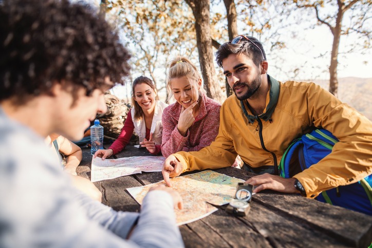 Hikers sitting on the bench at the table in the woods and looking at map