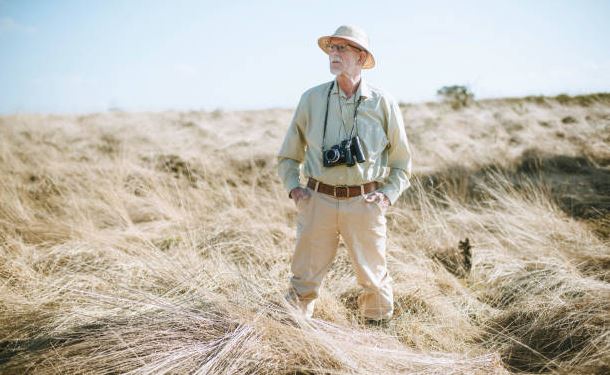 senior-tourist-with-camera-and-binocular-in-field