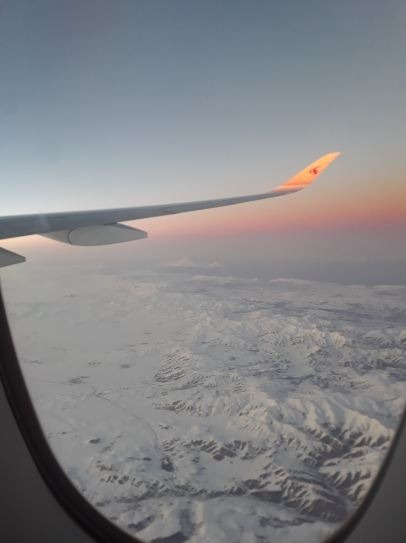 purple and pinkish sunset, airplane wing, aerial view of snowy mountains