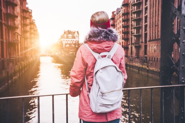 Rear view of adult woman tourist with white backpack enjoying sunset