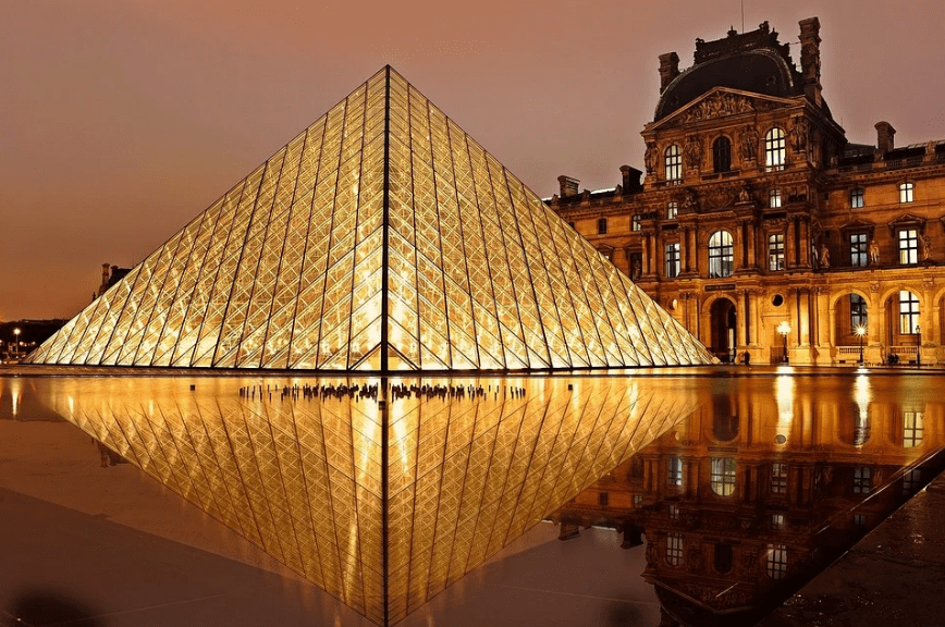 a glowing Louvre Museum at night, and a building at its side