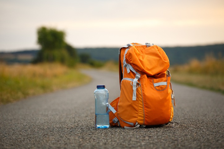 A backpack for an orange camera and a bottle of water on an asphalt road