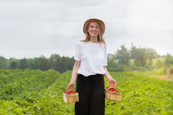 Happy smiling young blonde girl in a white t-shirt and hat on a strawberry field