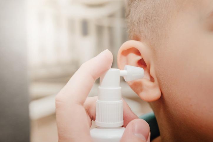 A parent cleaning the ears of a small child with a spray bottle